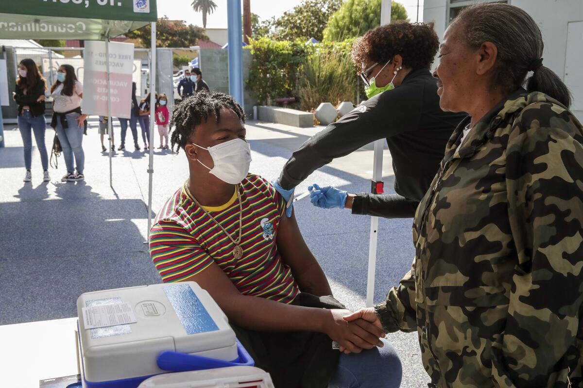 A teenage boy holds his mother's hand while getting a COVID-19 shot.