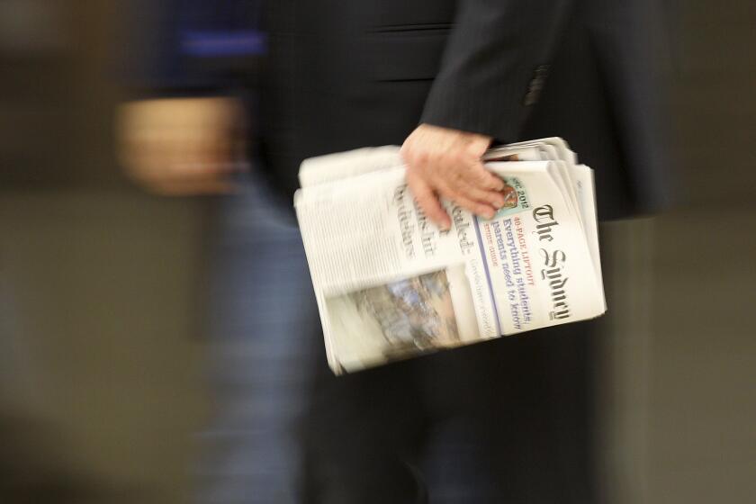 A man carries the Sydney Morning Herald newspaper as he walks through a train station.