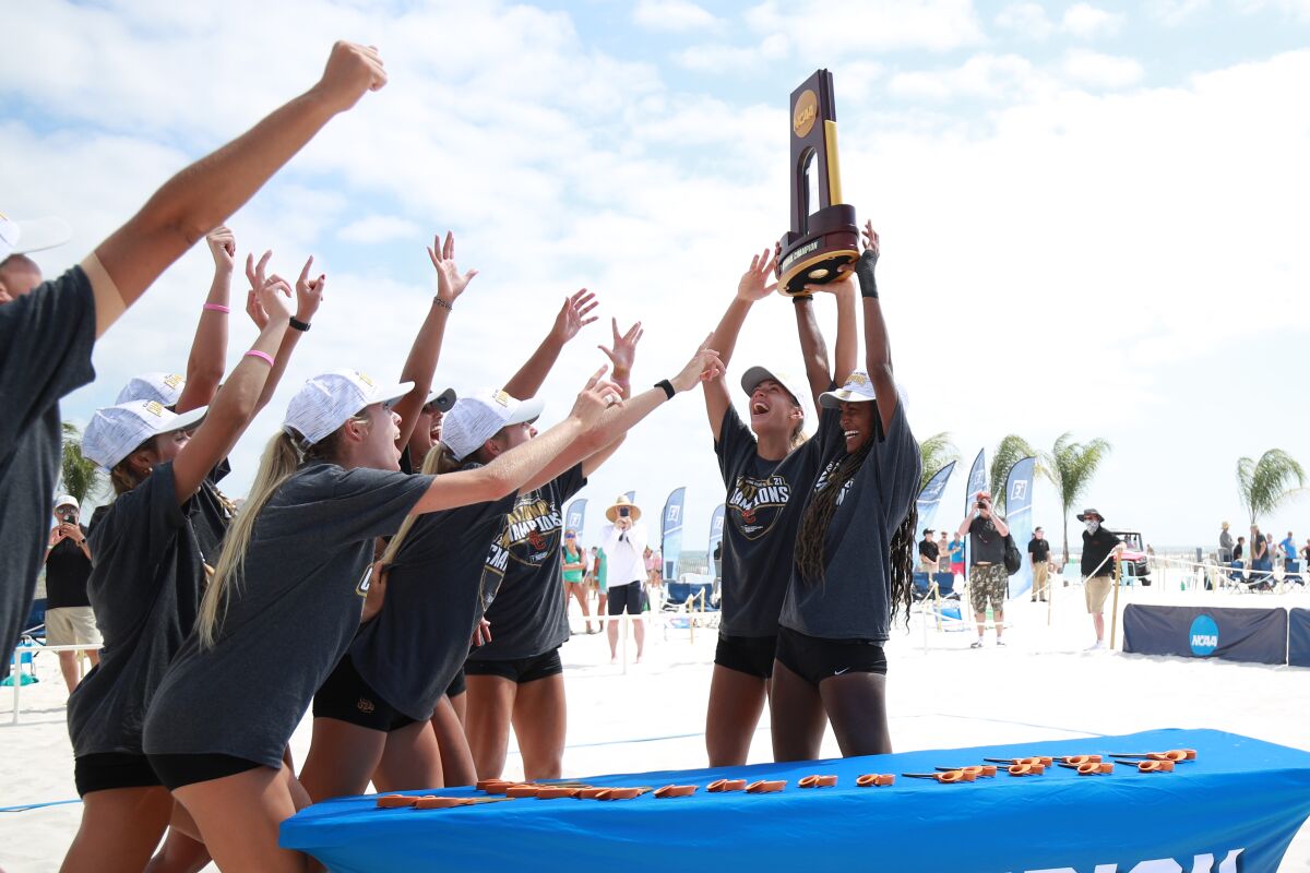 USC beach volleyball player Joy Dennis, right, helps lift the NCAA beach volleyball championship trophy.