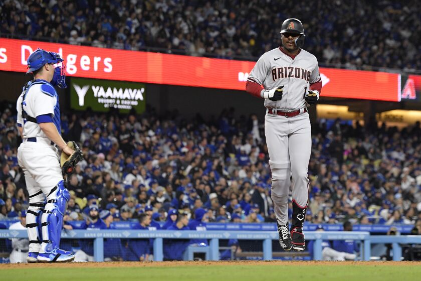 Arizona Diamondbacks' Kyle Lewis, right, scores after hitting a two-run home run as Los Angeles Dodgers catcher Will Smith stands at the plate during the eighth inning of a baseball game Friday, March 31, 2023, in Los Angeles. (AP Photo/Mark J. Terrill)