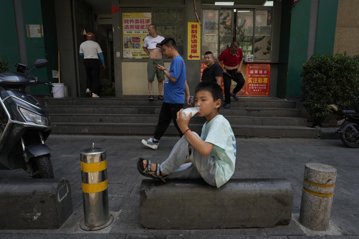 Child drinking out of a bottle outside a Beijing shop