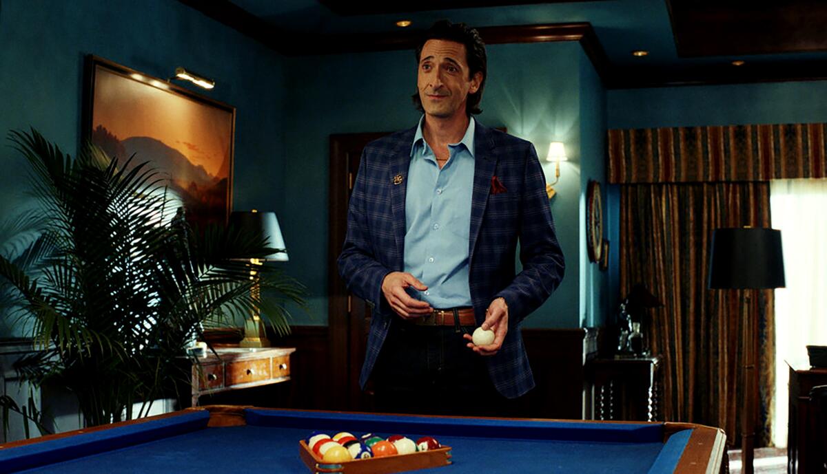 Adrien Brody stands by a pool table in a richly appointed office in "Poker Face,"