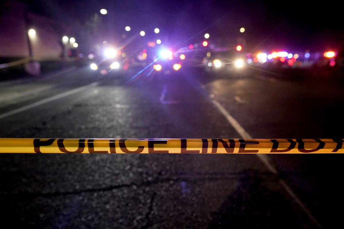 Police tape blocks a road where police lights are flashing