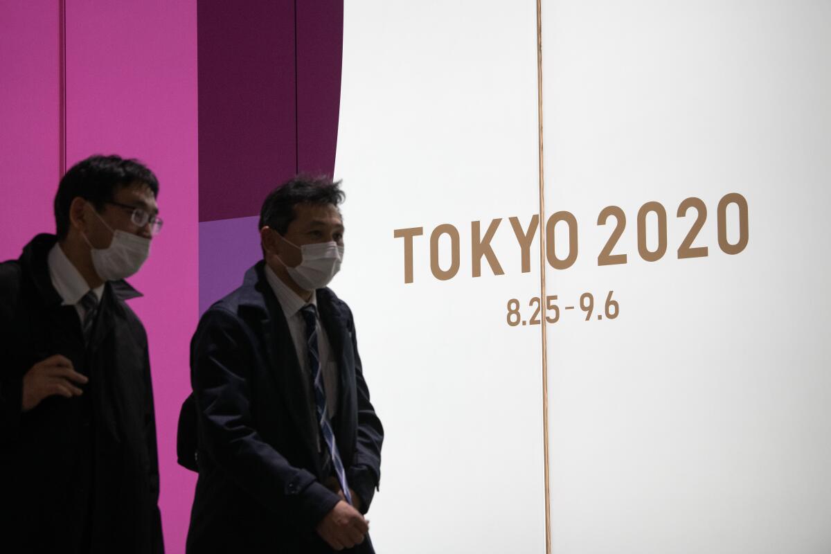 Two people in Tokyo pass a sign promoting the now postponed Summer Olympic Games.