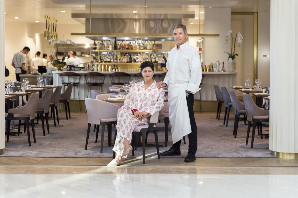 A woman sitting and a man in chef's whites standing in front of their restaurant.