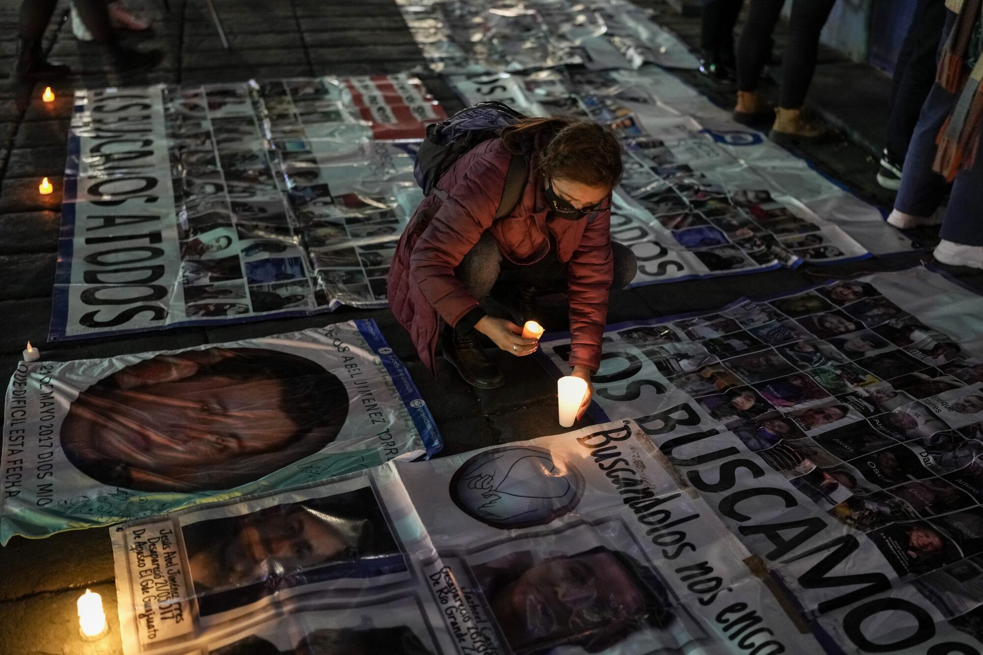 A woman places a candle alongside one of the missing persons posters on the ground 