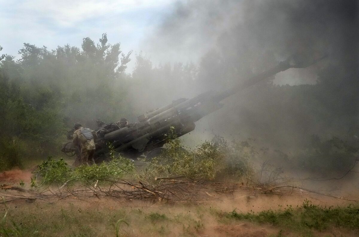 Ukrainian soldiers fire heavy artillery in a dusty field