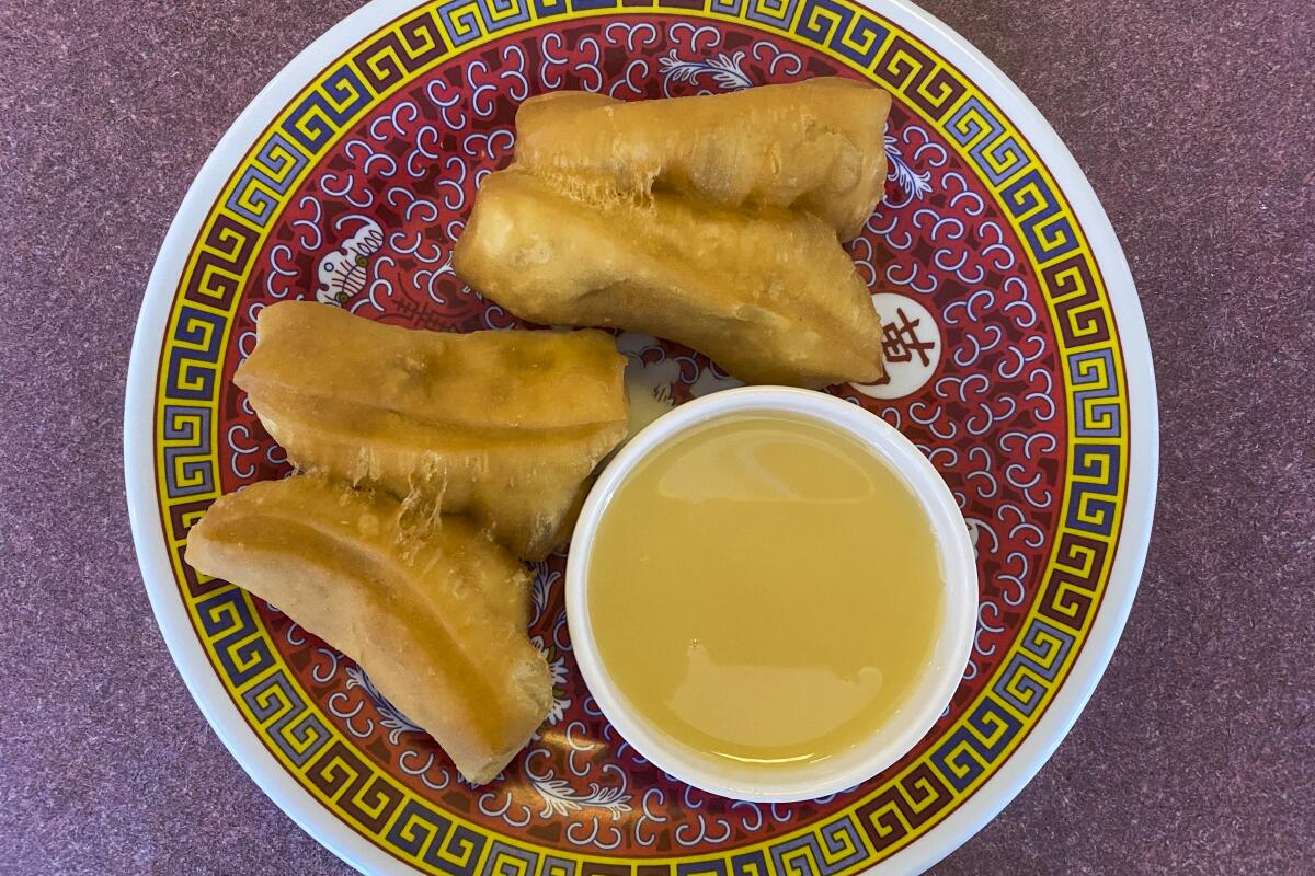 Chinese doughnuts on a patterned plate with a bowl of condensed milk for dipping.