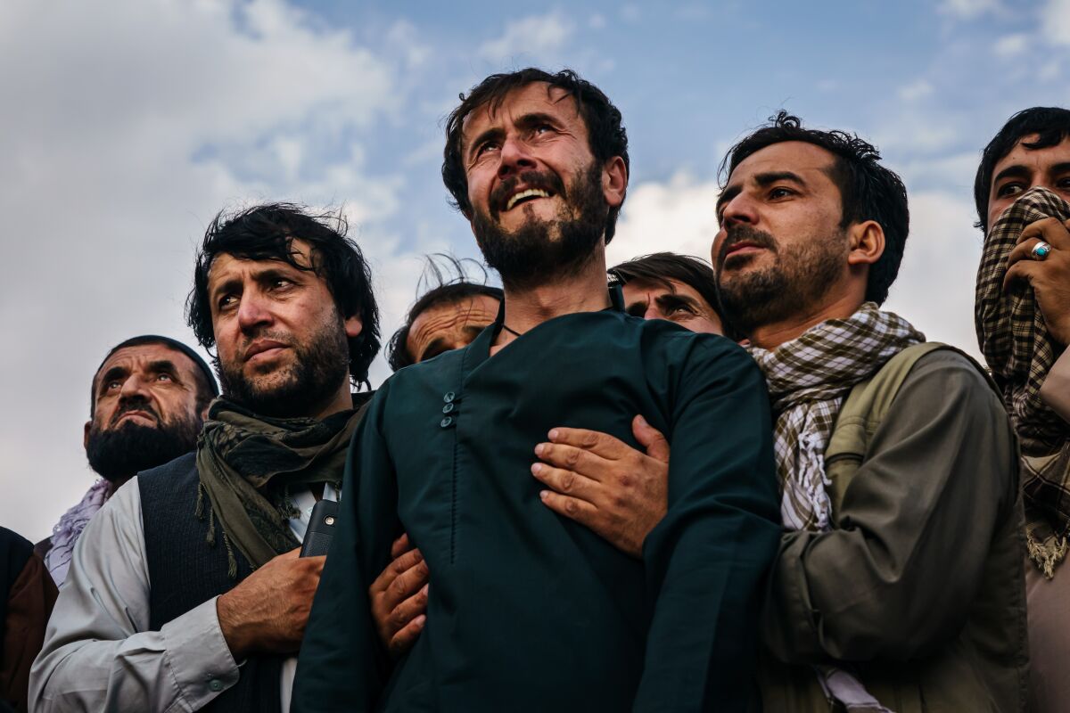 Ramal Ahmadi, center, is supported by relatives as he weeps while watching warplanes circle the skies above. 