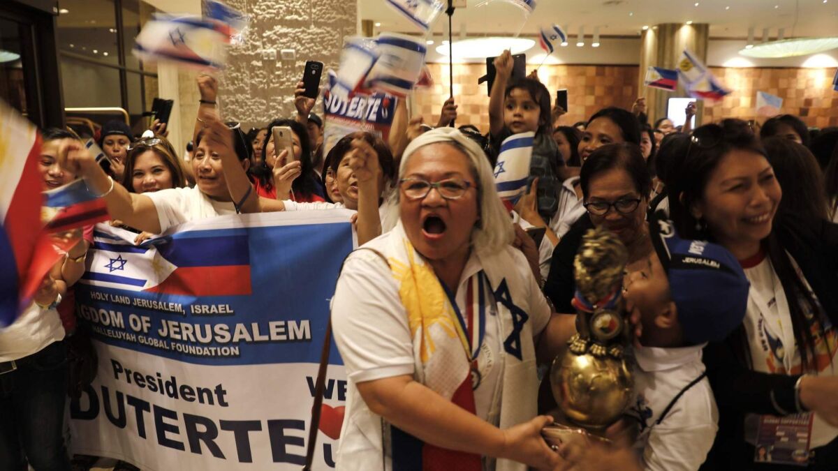 Members of the Filipino community in Jerusalem wave Philippine and Israeli flags as they await the arrival of their president, Rodrigo Duterte.