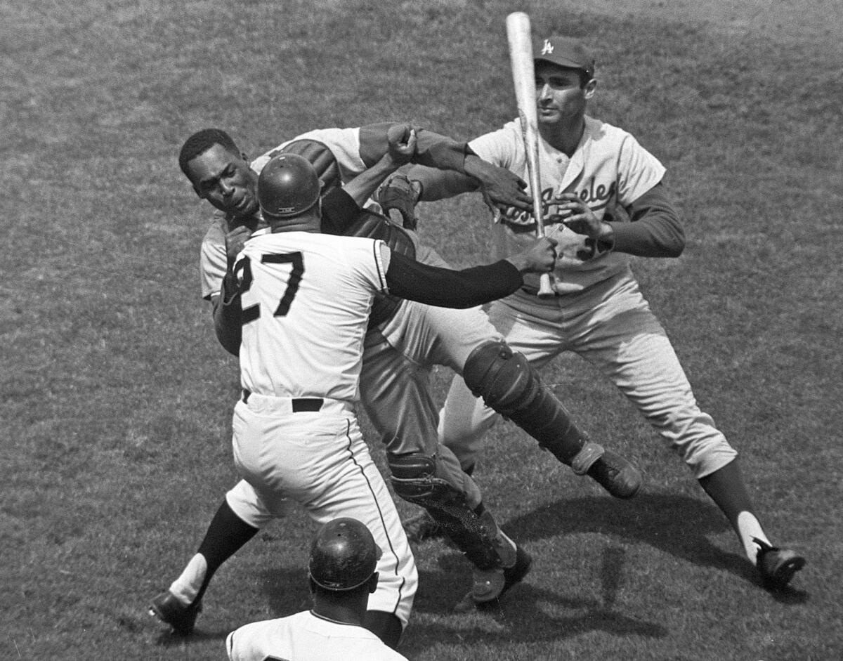 San Francisco pitcher Juan Marichal (27) swings a bat at Dodgers catcher John Roseboro as Dodgers pitcher Sandy Koufax, right, tries to break it up on Aug. 22, 1965.