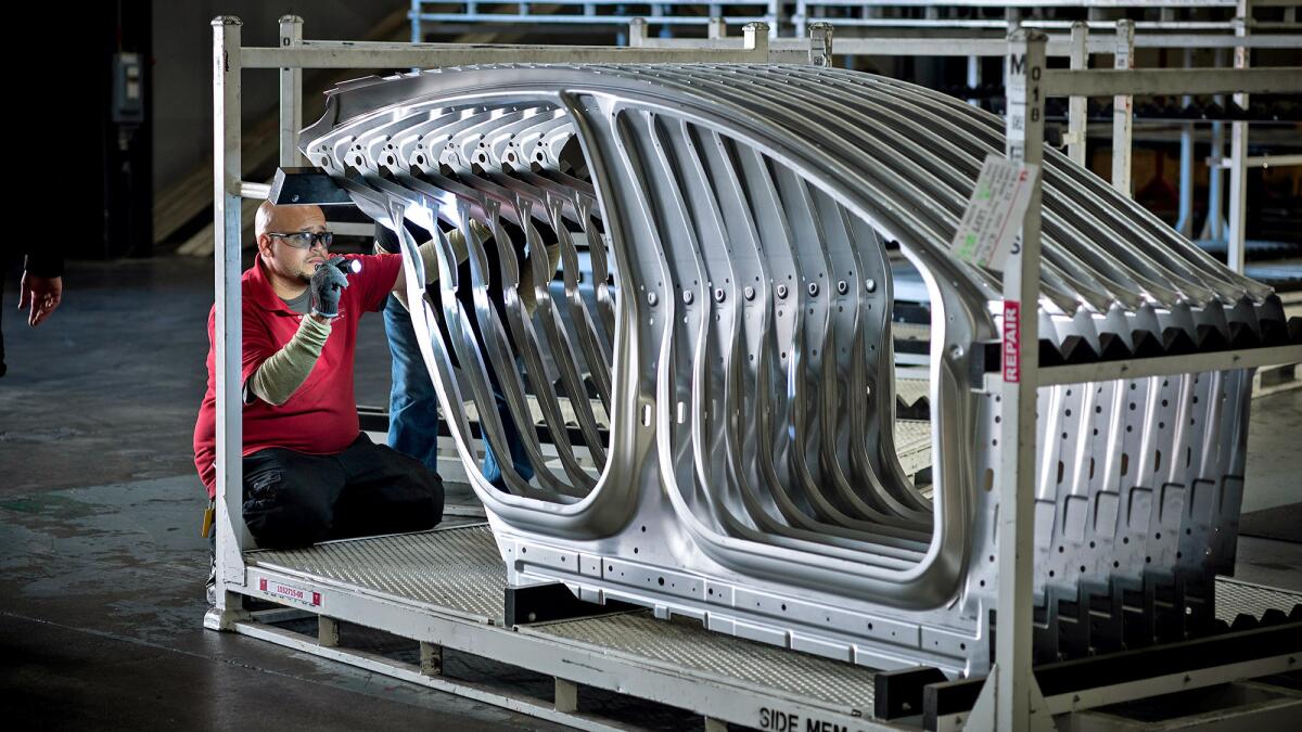 Scenes at the Tesla car factory include a worker checking the detail of finishing on aluminum parts.