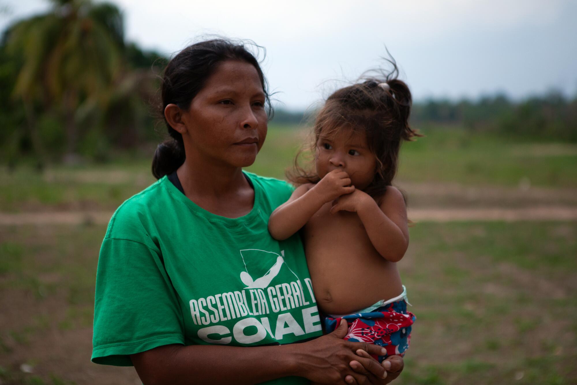 A woman with dark hair and a green T-shirt holds a young girl 