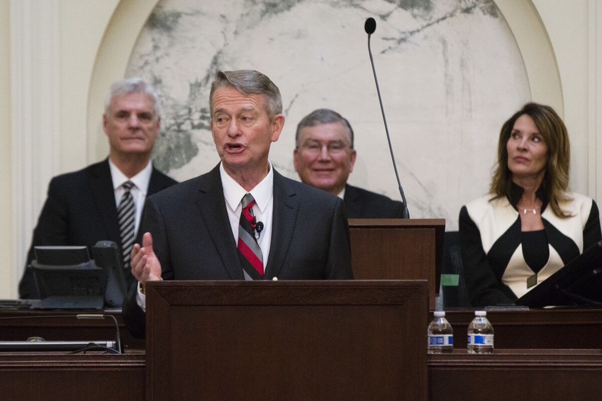 Brad Little speaks at a lectern. Several people stand in the background.