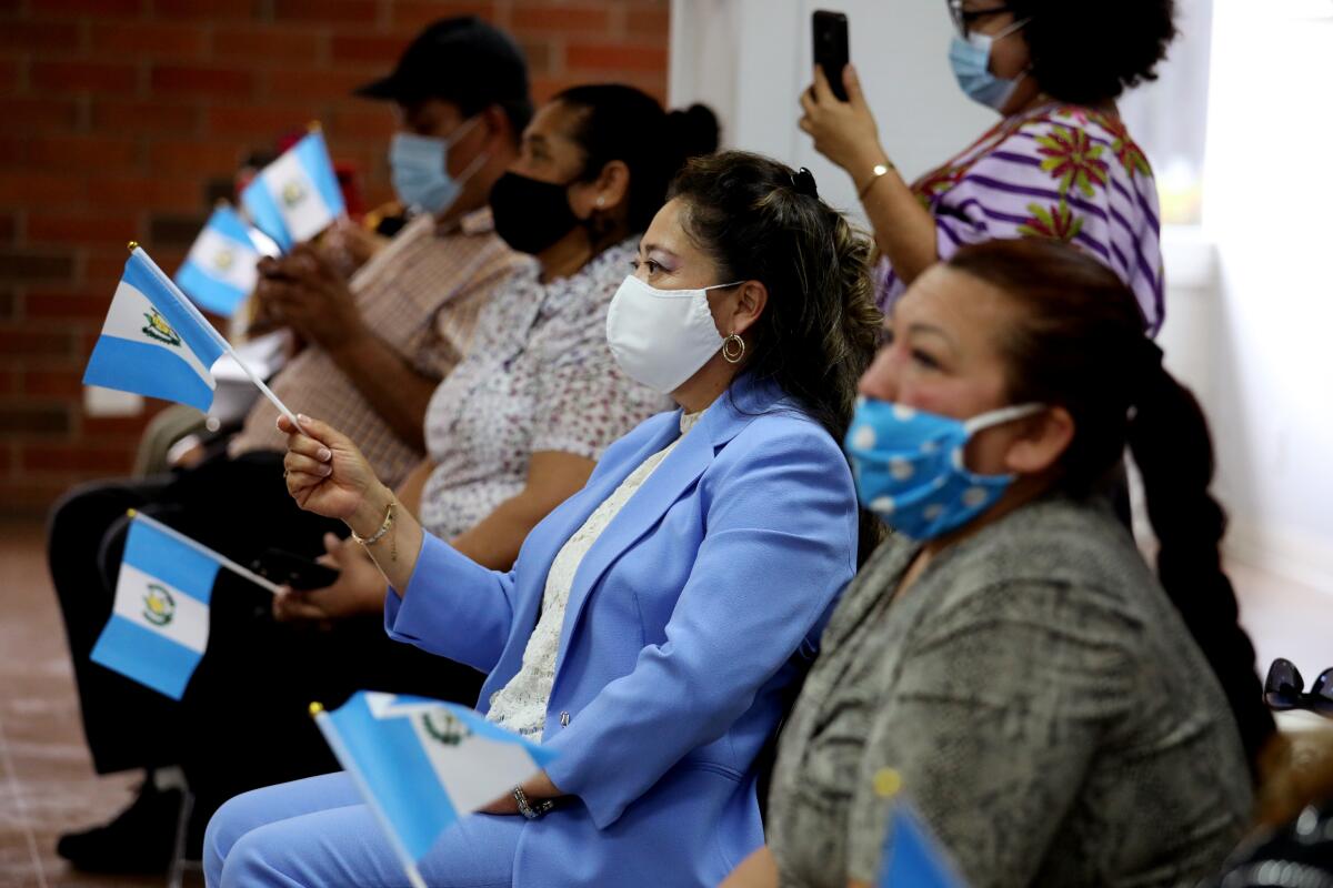 A row of seated people wearing masks and holding the Guatemalan flag