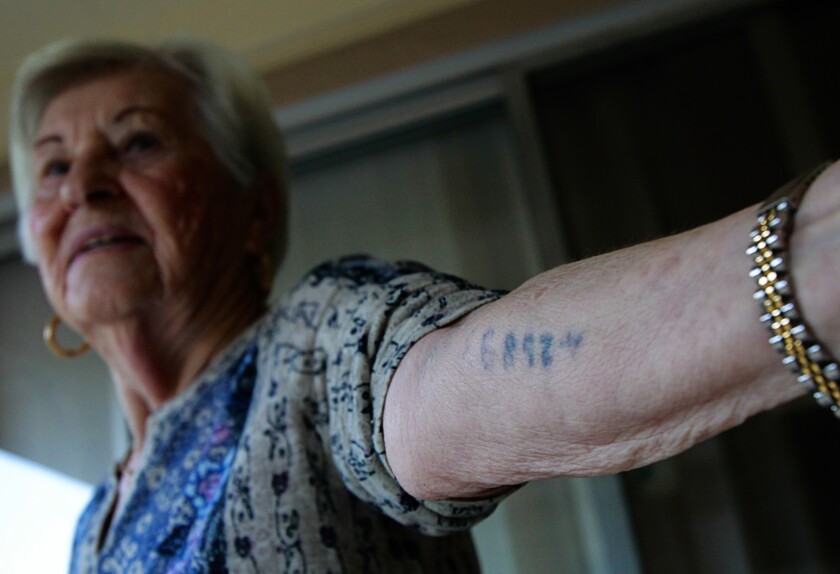 A woman holds out her forearm, tattooed by the Nazis with an identification number 
