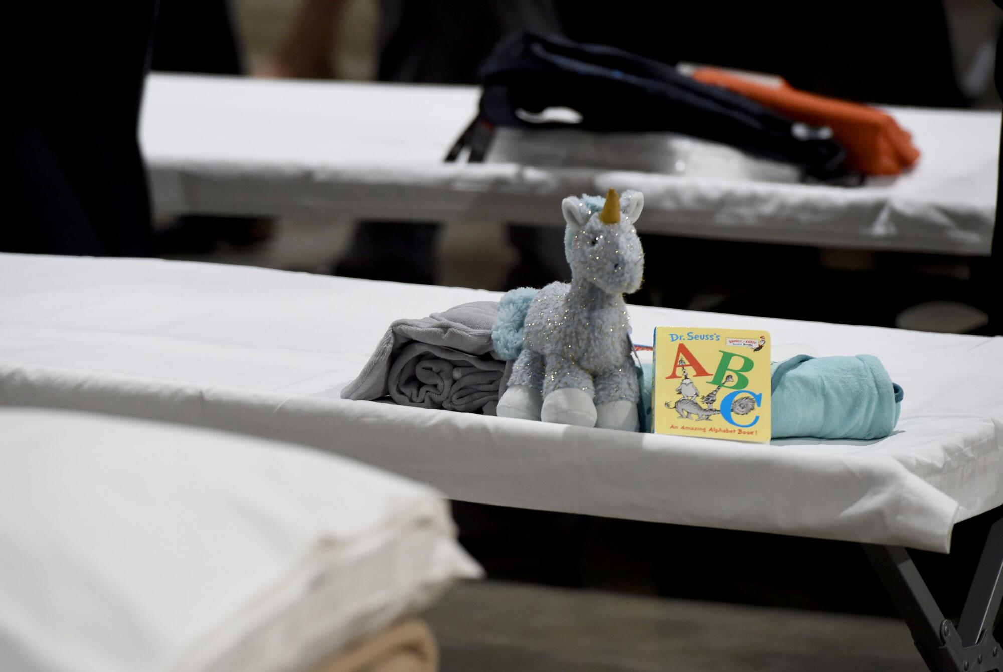 A stuffed unicorn, Dr. Seuss book and blankets sit on top of a white cot