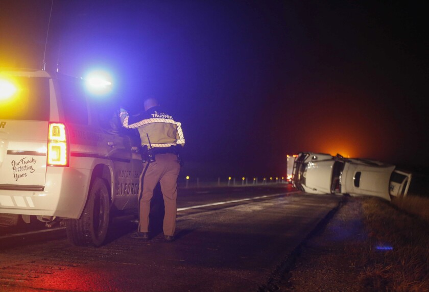 An Iowa State Patrol trooper works the scene of an overturned semi truck along the westbound shoulder of Interstate 80 near Anita, Iowa, on Wednesday, Dec. 15, 2021, after a band of intense weather crossed through the area. (Bryon Houlgrave/The Des Moines Register via AP)