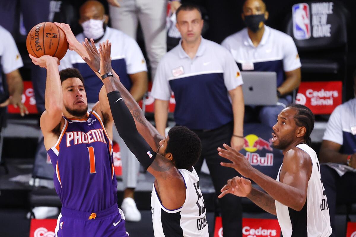 Phoenix Suns guard Devin Booker, left, shoots over Clippers forwards Paul George, center, and Kawhi Leonard at the buzzer.