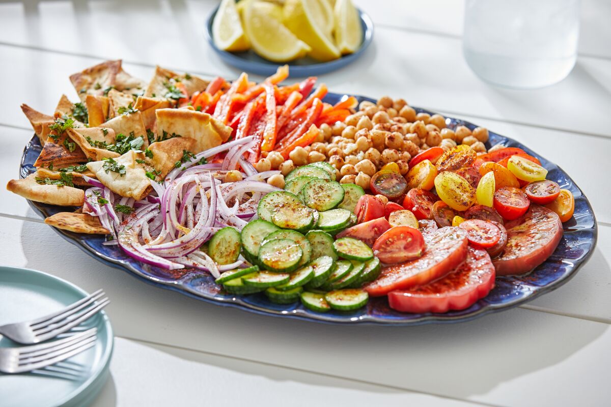 Pita bread, peppers, red onion, chickpeas, cucumbers and tomatoes are drizzled with dressing on a  platter.