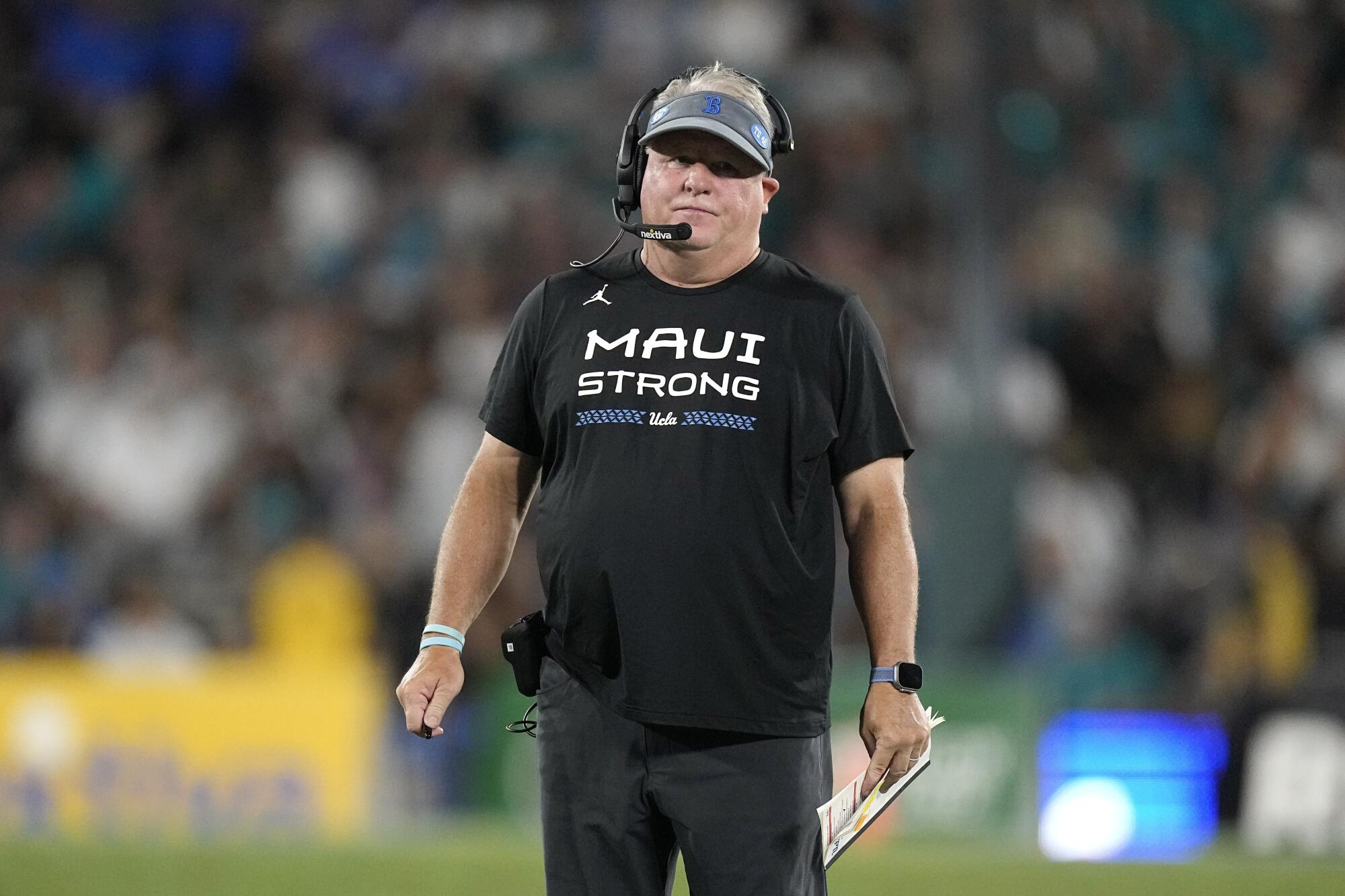 UCLA coach Chip Kelly stands on the field during the first half of a game.