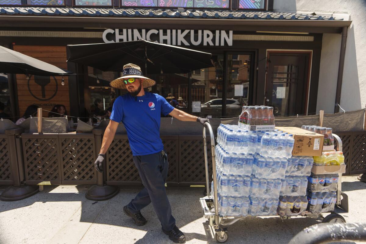 A man pulls a cart loaded with cases of beverages in front of a business