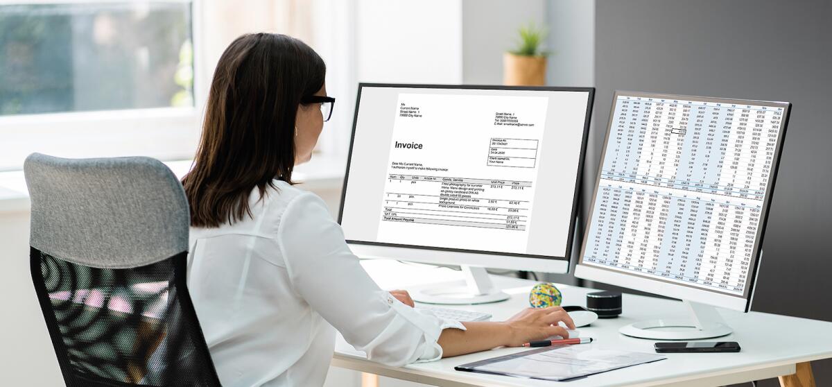 A woman studying an invoice and spreadsheet on a pair of screens