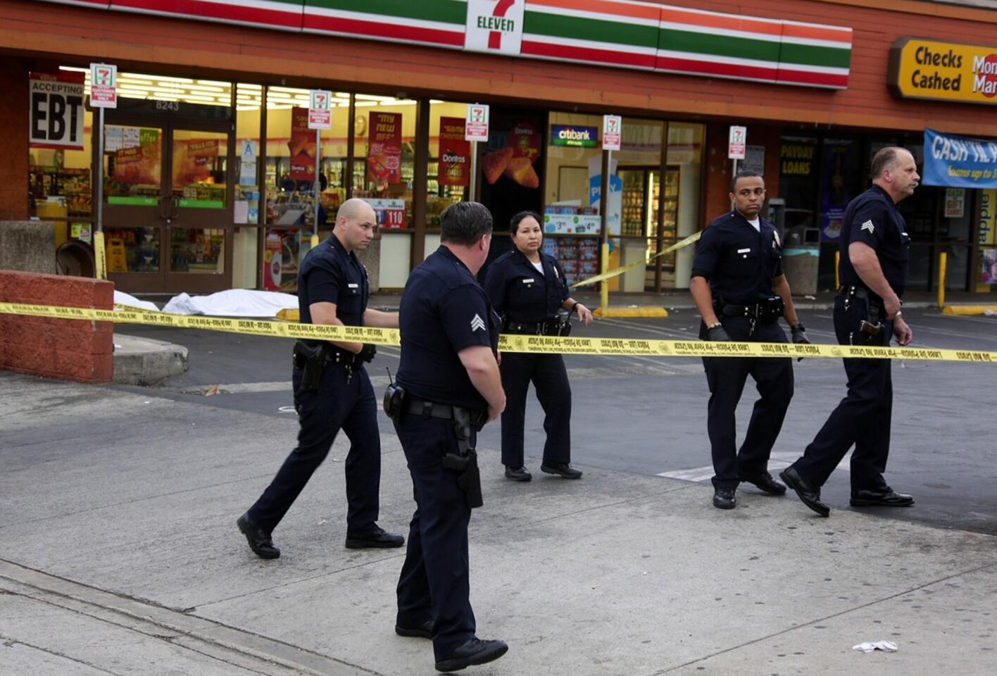 Police officers investigate a shooting at a 7-Eleven in Van Nuys July 17. Two men were found dead at the scene; a third was injured.
