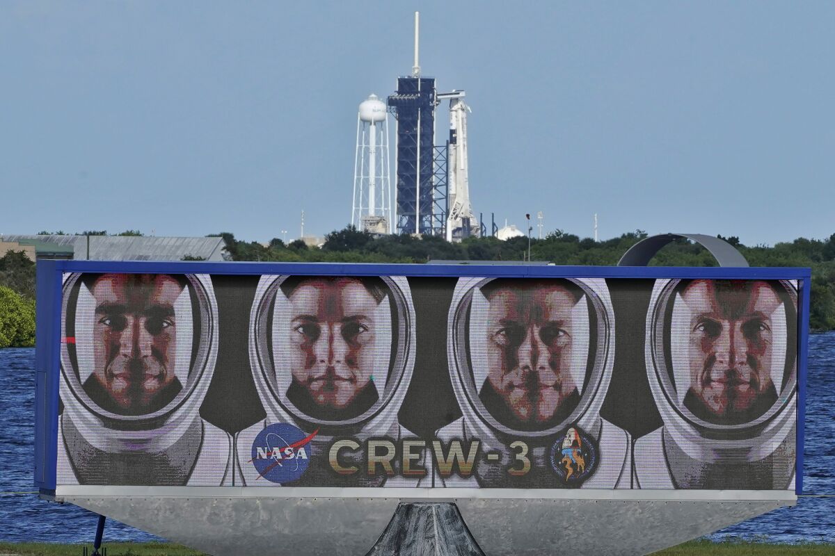 FILE - The official portraits of astronauts, from left, Raja Chari, Kayla Barron, Matthias Maurer, of Germany, and Tom Marshburn, are displayed as a SpaceX Falcon 9 rocket with the crew dragon capsule attached sits on Launch Pad 39-A at the Kennedy Space Center in Cape Canaveral, Fla., Friday, Oct. 29, 2021. On Thursday, Nov. 4, 2021, officials announced SpaceX's next astronaut flight is off until at least next week as more bad weather looms, and as flight surgeons continue to monitor the “minor medical issue” affecting one of the four astronauts. (AP Photo/Chris O'Meara, File)