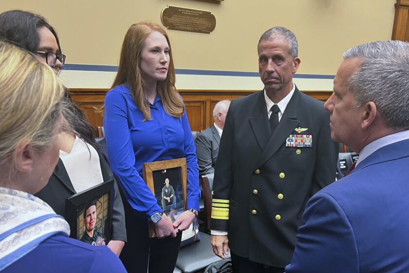 Amber Sax, center, holds a photo of her late husband, Marine Corps MV-22B pilot Capt. John Sax, as she and other family members who have lost service members to Osprey crashes talk with Vice Adm. Carl Chebi, Commander of U.S. Naval Air Systems Command, center right, and Peter Belk, acting Assistant Secretary of Defense for Readiness, right, before a hearing on the programs safety record, Wednesday, June 12, 2024, on Capitol Hill in Washington. (AP Photo/Tara Copp)