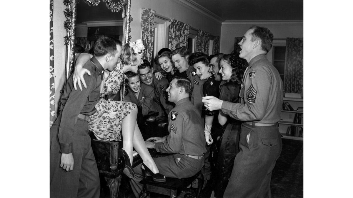 A group of young men and women gather around a piano.