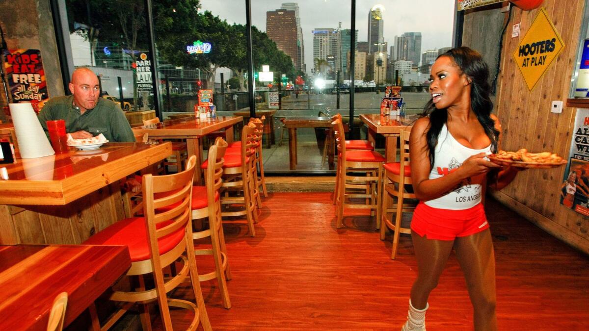 Customer Matt Thomas sits at a table at a Hooters restaurant in Los Angeles as employee Keiana Martinez delivers a meal to another customer. The Hooters chain was sued because its website did not comply with the Americans with Disabilities Act.