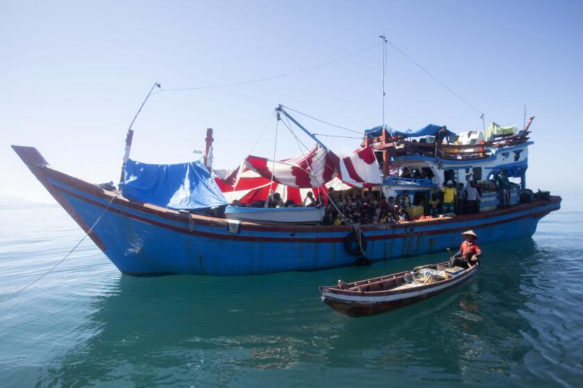 A local fisherman navigates past a boat carrying Rohingya refugees anchored in the waters near the coast of Labuhan Haji, Aceh province, Indonesia, Tuesday, Oct. 22, 2024. (AP Photo/Binsar Bakkara)