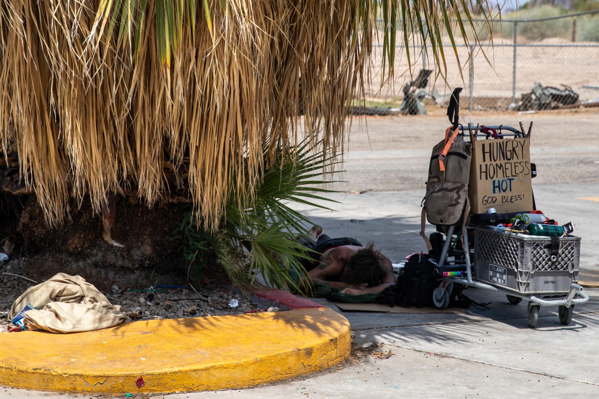 A homeless man sleeps in the shade of a tree in Blythe. Next to him is a cart of his belongings.