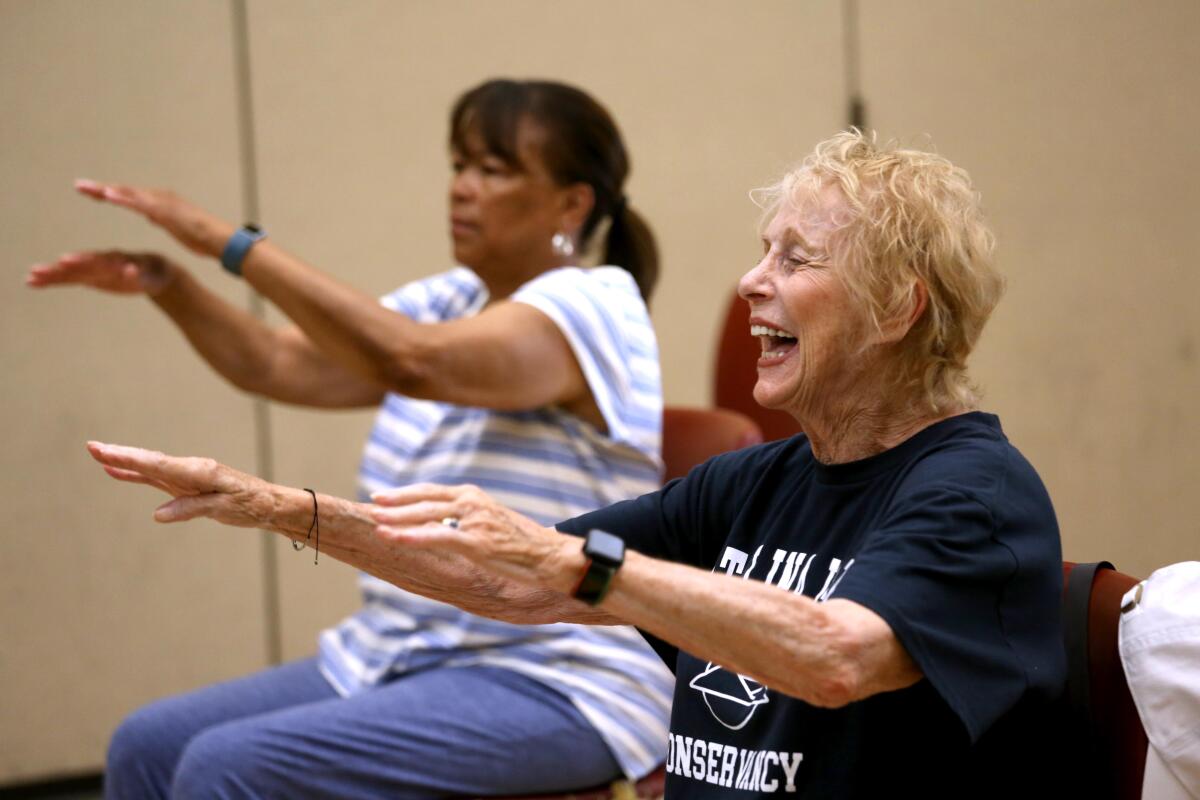     Judith Kendall, right, smiles as she sits with her arms out in front of her in class.