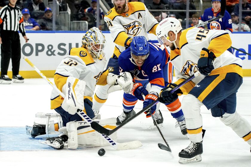 New York Islanders left wing Anders Lee (27) and Nashville Predators defenseman Alexandre Carrier (45) fight for the puck as Predators goaltender Kevin Lankinen (32) guards the goal during the second period of an NHL hockey game, Friday, Dec. 2, 2022, in Elmont, N.Y. (AP Photo/Julia Nikhinson)