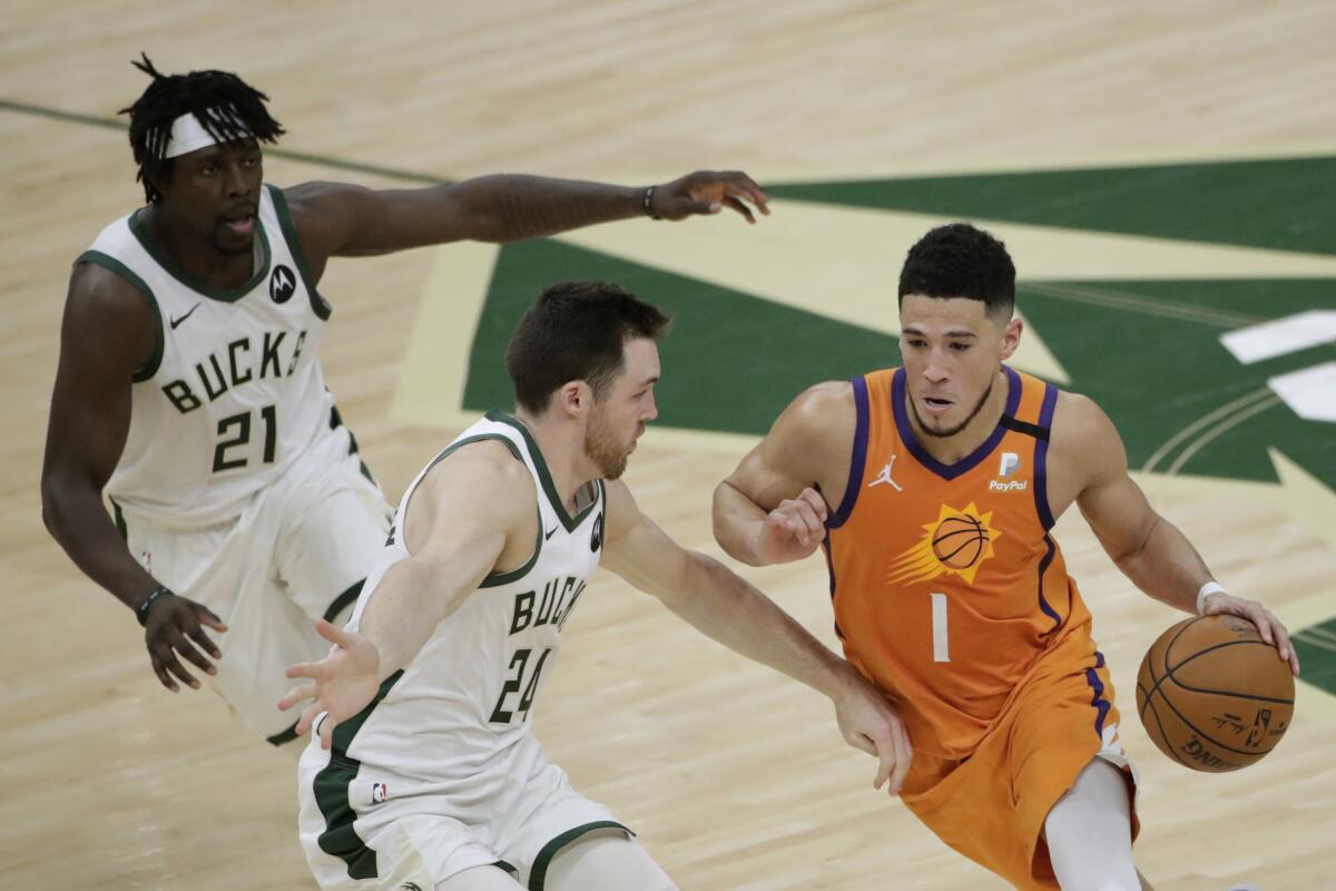 Phoenix Suns guard Devin Booker drives past Milwaukee Bucks guard Pat Connaughton and guard Jrue Holiday.