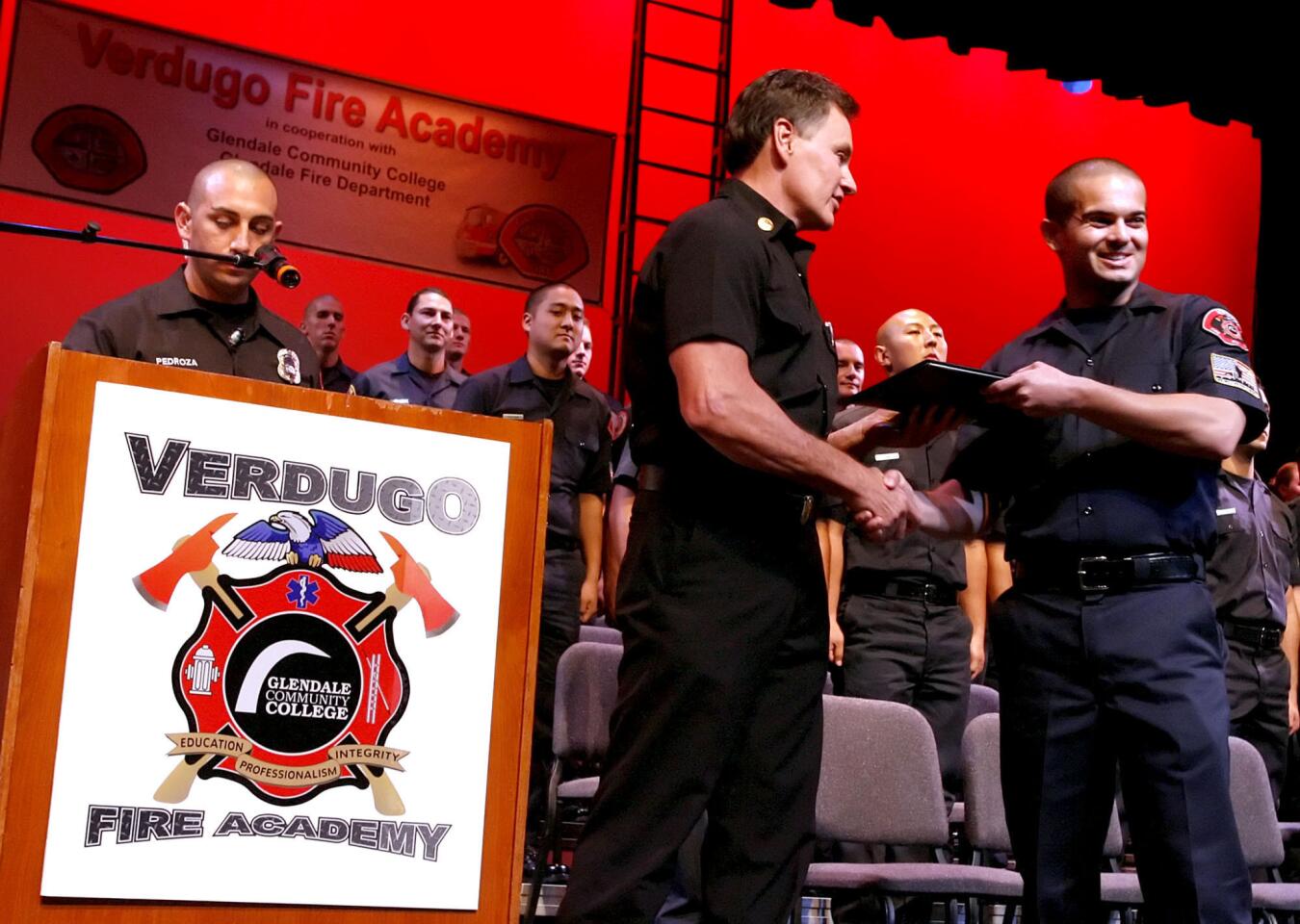 Glendale firefighter and fire academy instructor Gilbert Pedroza, left, calls out graduate names as Cadet Brian Rich, right, gets his graduation certificate from chief Sam DiGiovanna, center, at the Verdugo Fire Academy Graduation Ceremony for Class XIV at Glendale College on Saturday, January 7, 2012. Forty-five cadets graduated.