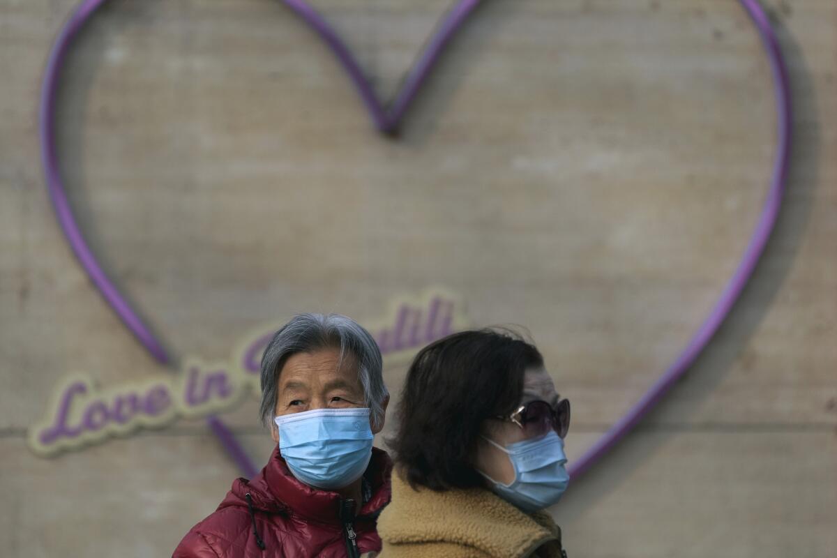 Dos mujeres con mascarilla se ven ante un adorno con forma de corazón en Beijing