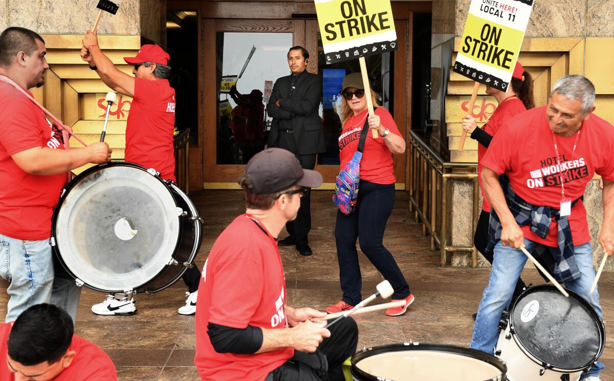 People wearing red shirts hold picket signs and bang drums outside a building.