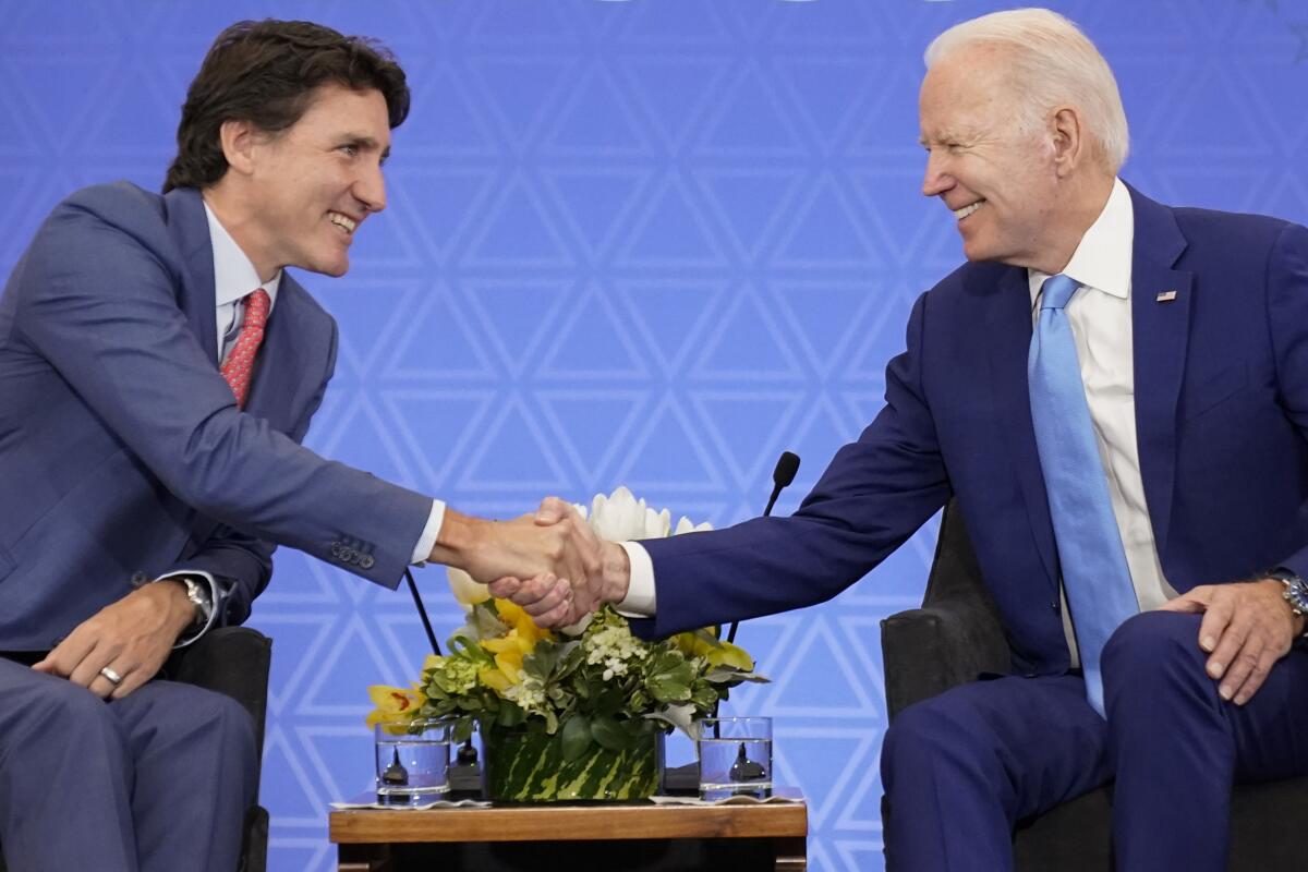 Justin Trudeau, left, and Joe Biden shake hands while seated