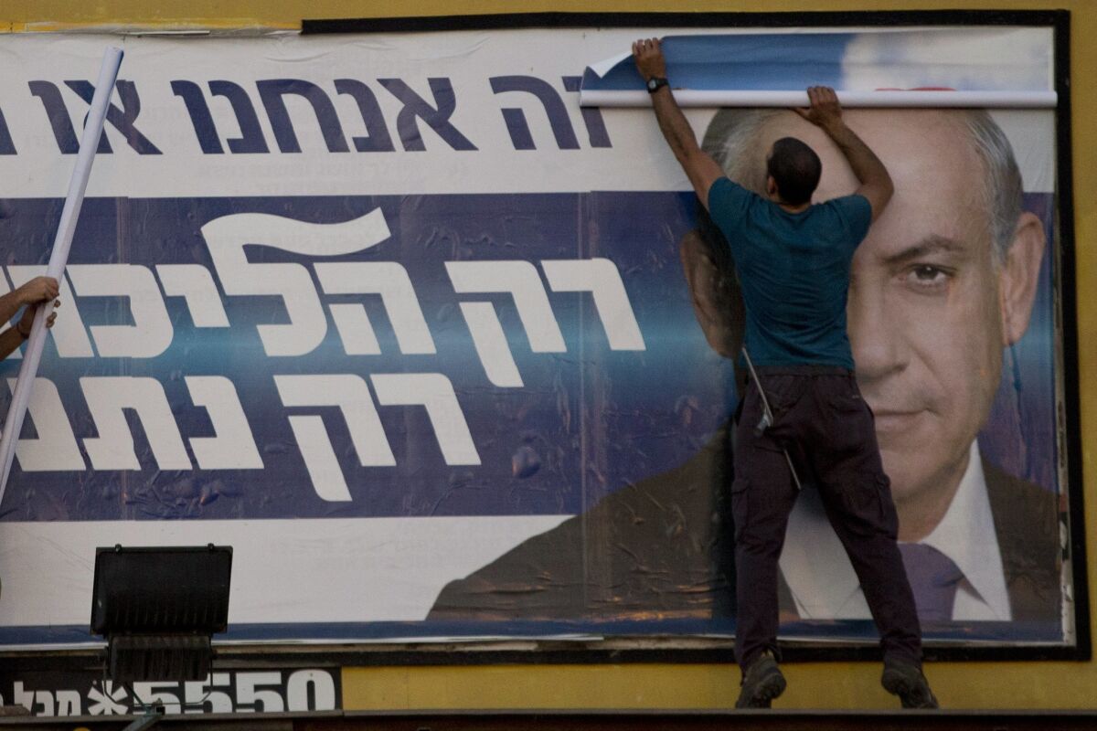 Workers in Israel remove an election campaign billboard showing Prime Minister Benjamin Netanyahu. With the election over, Netanyahu went on U.S. television Thursday to try to walk back several controversial remarks.