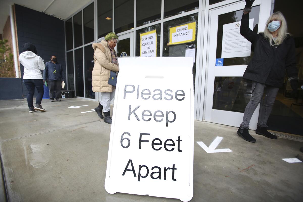 FILE - A sign asks those getting vaccinated to keep 6 feet apart during the vaccination event