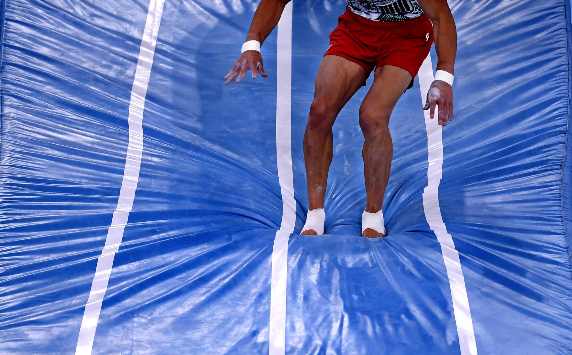 A closeup of a gymnast's lower half making a depression in a blue mat.