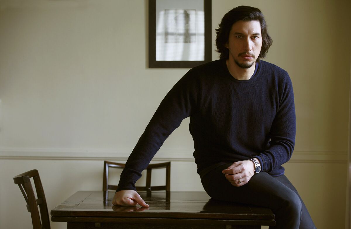 Actor Adam Driver dressed in black, sitting on a table