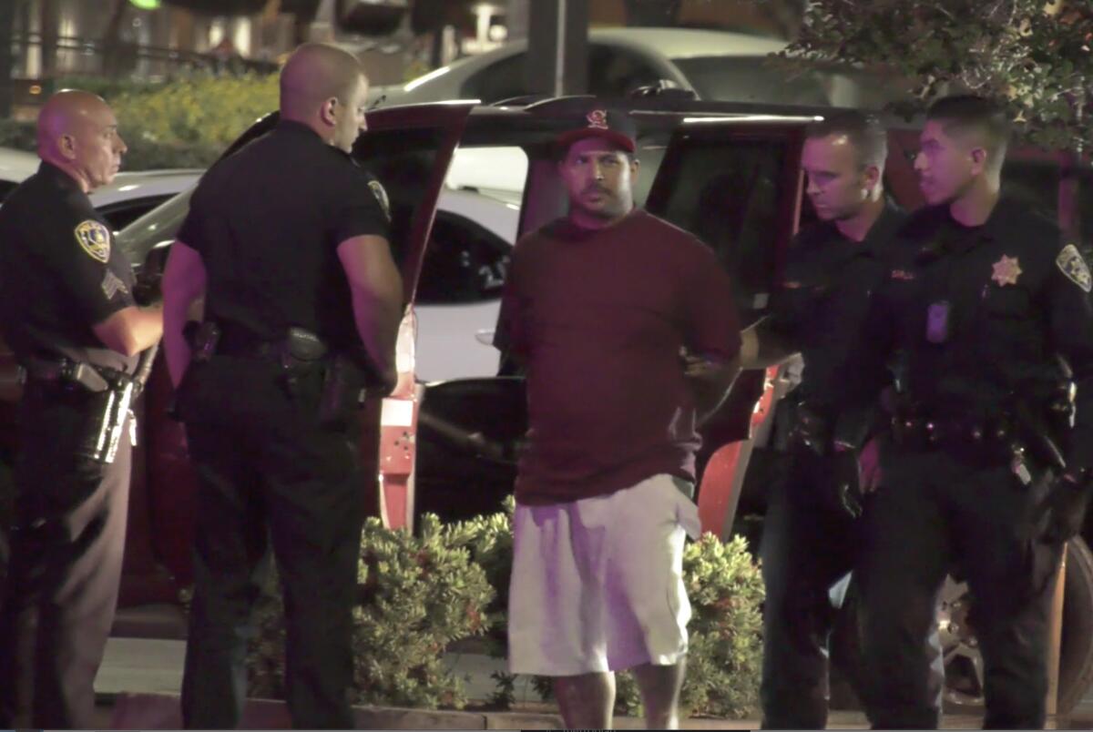 A man with his hands behind his back stands amid police officers.