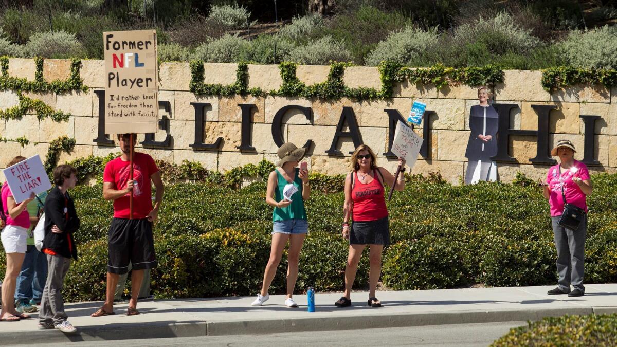 A group of protesters, accompanied by a cutout of Hillary Clinton, assembles outside the entrance to The Resort at Pelican Hill on Monday to show their disapproval of Vice President Mike Pence, who was attending a political fundraiser there.