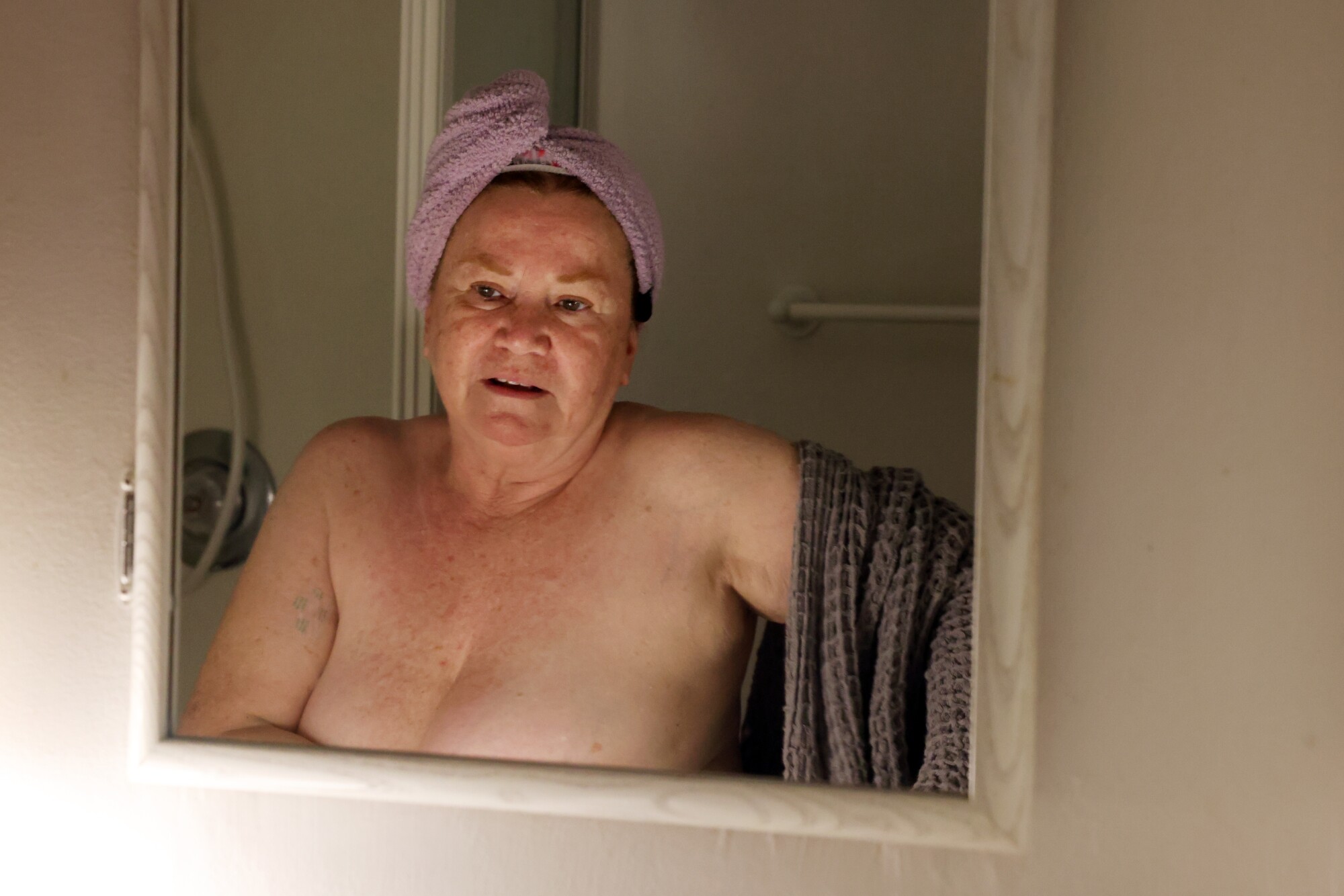 A woman with a towel on her head looks into a mirror 