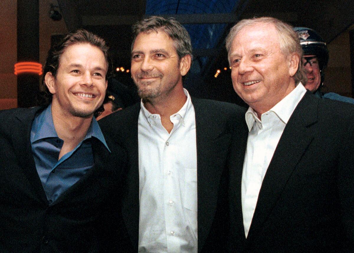 Three men wearing suits stand together and smile.