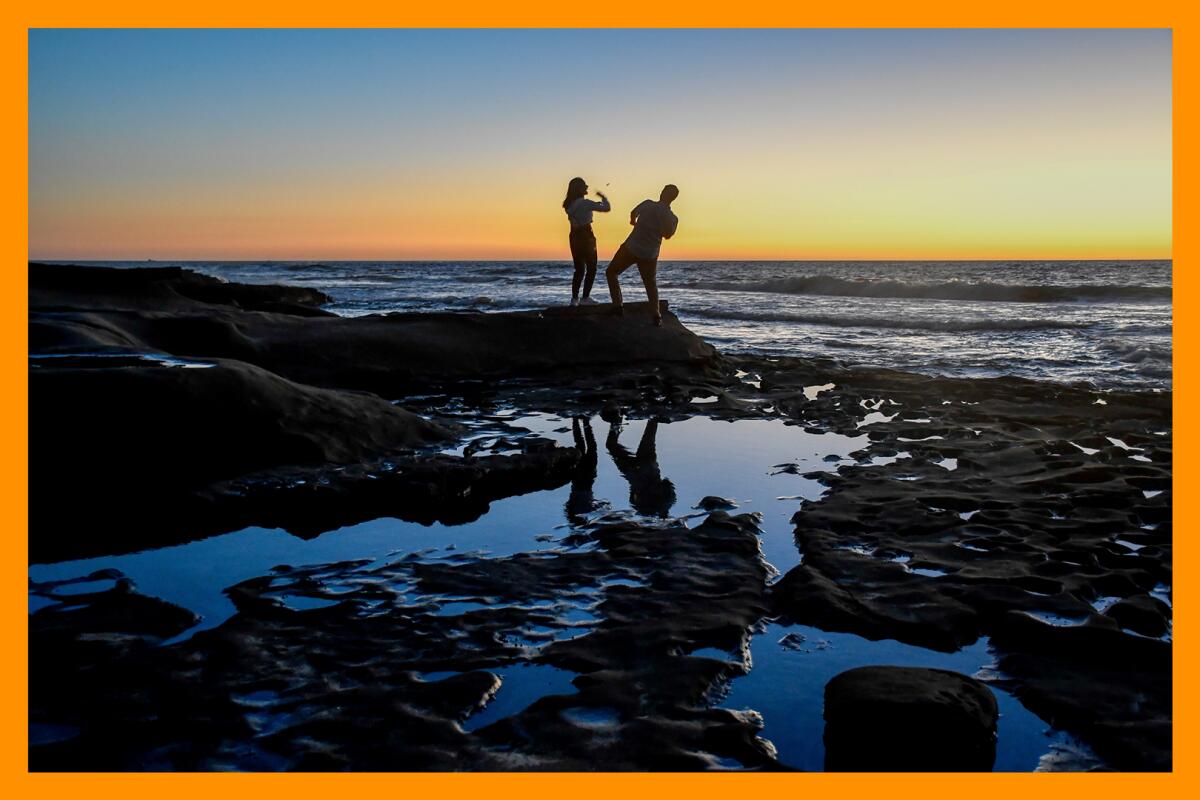 Two people visiting a tide pool are silhouetted against the setting sun.